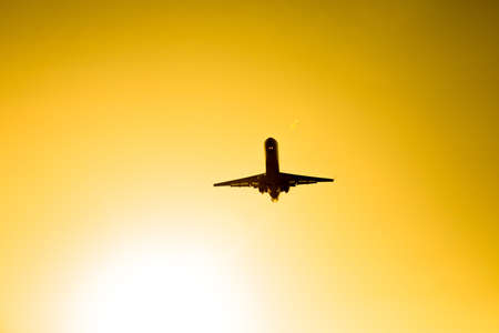 Flying airplane silhouette in the orange sky sunset.の写真素材