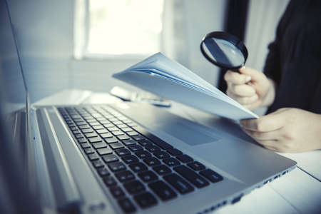 Woman holding magnifying glass over notebook, search concept.