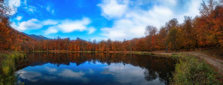 Beautiful autumn landscape. Lake, yellow and red trees by the lake. Reflection in water. Blue sky. Sunny autumn day.の写真素材