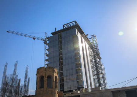Cranes in construction process on top of office building construction over clear cloudless blue sky.