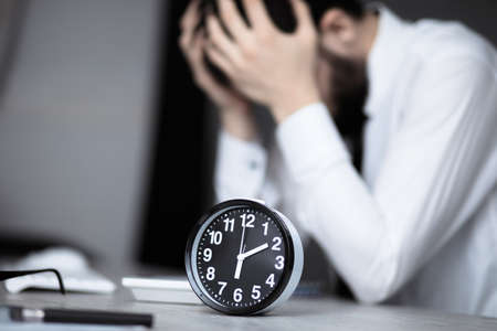 sad man with vintage clock on office deskの写真素材