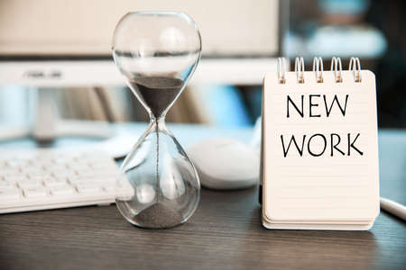 new work text on notepad with hourglasses and keyboard on tableの写真素材