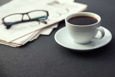 glasses on newspapers with cup of coffee on desk