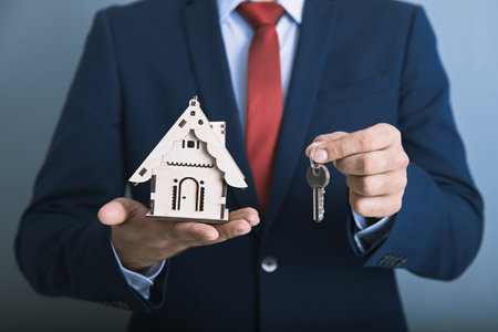man hand holding house key with house modelの写真素材
