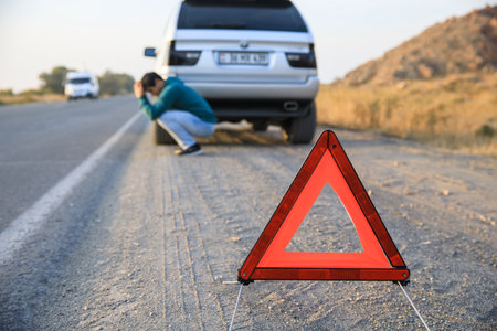 Red emergency stop sign and broken silver car on the roadの写真素材
