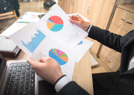 man holding graph with computer on working tableの写真素材