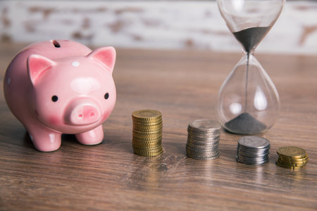 hourglass with coins and piggy bank on tableの写真素材