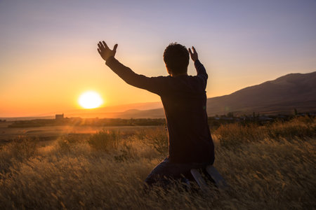 man with hands raised in the sunset concept for religion