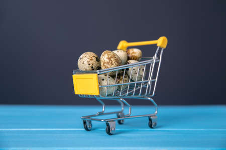 Raw quail eggs in mini shopping cart on blue bakgroundの写真素材