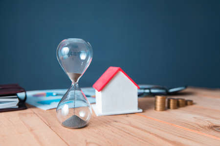 hourglass and house model with coins on the table