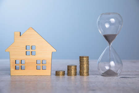 house model with hourglass and coins on tableの写真素材