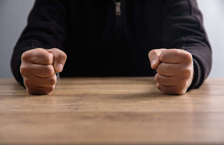 man fists clenched on a wooden tableの写真素材