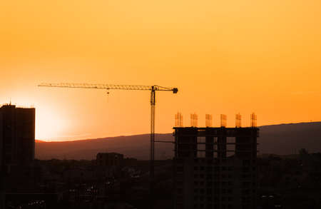 Construction site at sunrise. Industrial construction cranes and building silhouettes over sun at sunriseの写真素材