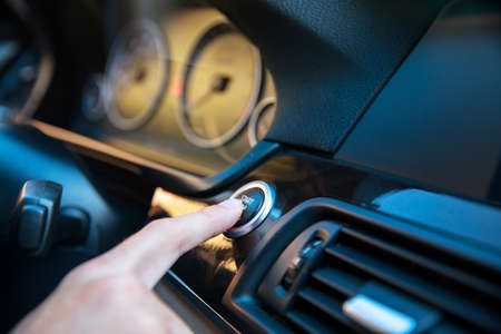 man finger presses the start stop button on a car