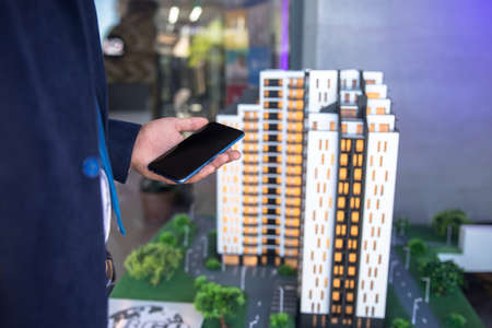 man holding phone with house models on tableの写真素材