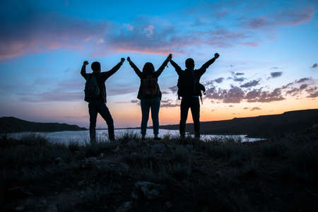 A group of people hiking success silhouette in mountains at sunset