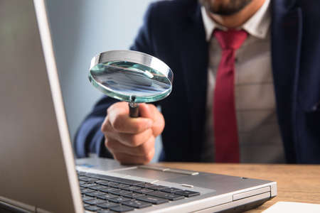 business man holding magnifier with laptop