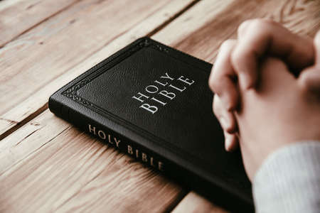 Christian man praying with hands crossed and Holy Bible