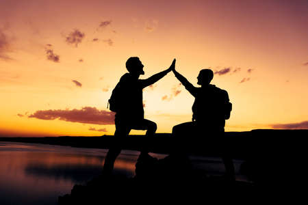 Silhouette of two people with success gesture standing on top of a mountainの写真素材