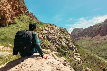 Young tourist with backpack sitting on the top of the mountainの写真素材