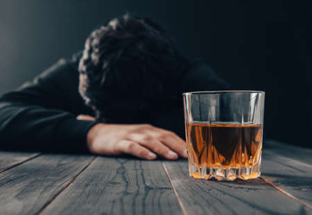 sad man with glass of alcohol on table
