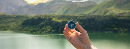 A man holds a compass against the backdrop of a lake and forestの写真素材