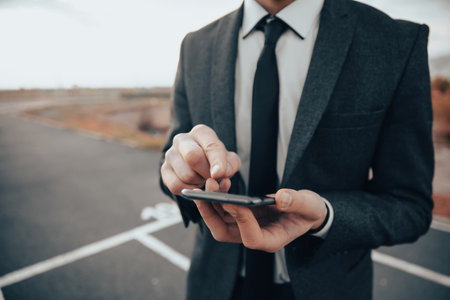 A man in a suit clicks on the phone screen on the streetの写真素材