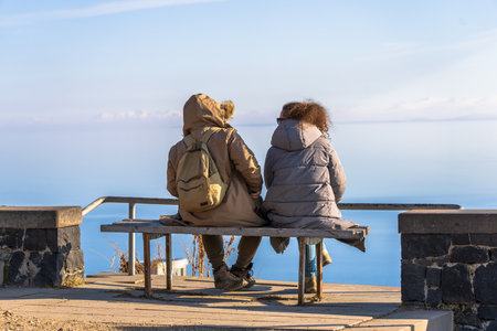 People sit on a bench by the lake during the dayの写真素材