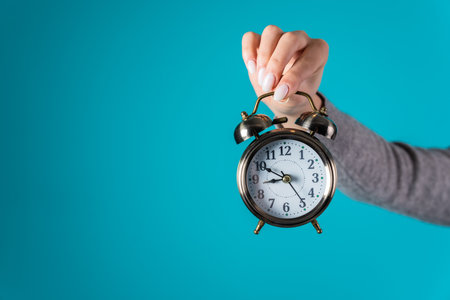Woman holding an alarm clock in her hand on a blue background