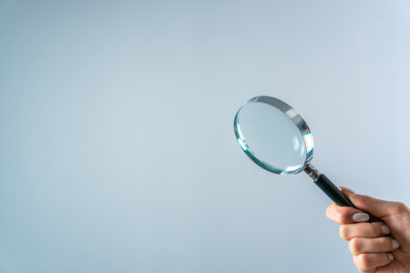 Young woman holding magnifier on gray backgroundの写真素材