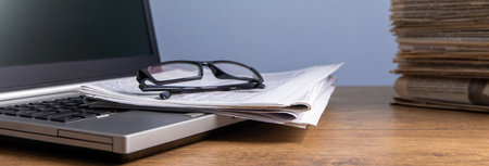 Glasses on notebook with stack of newspapers on the tableの写真素材