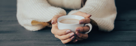 Young woman holding a cup of coffee in her hand at the tableの写真素材