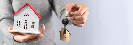 Young woman holding a wooden house and house keys in her handの写真素材