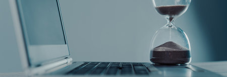 Laptop and hourglass on the tableの写真素材