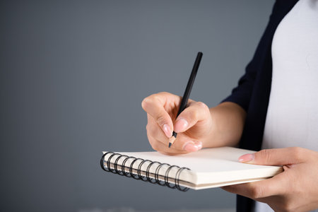 Woman writing in a notepad on a gray background