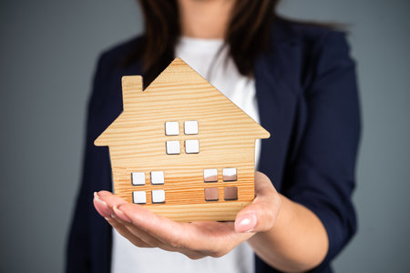 Woman holding a model of a house in her hand on a gray backgroundの写真素材