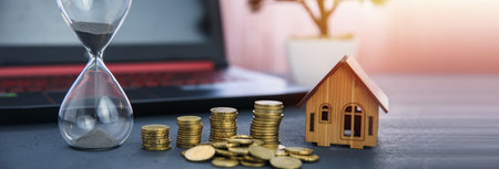 hourglass with coins and house model on deskの写真素材