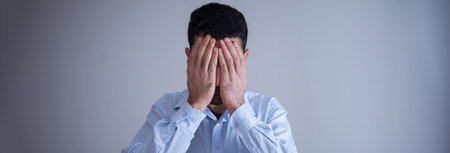 Man closed his face on gray wall background