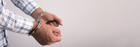 young man hand handcuffs on gray backgroundの写真素材