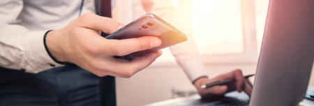 man hand phone with working computer on desk background