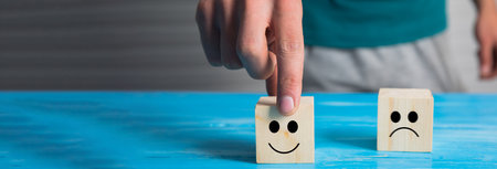 hand choose smiley face and blurred sad face icon on wood cubeの写真素材