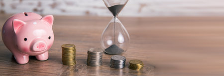 hourglass with coins and piggy bank on tableの写真素材