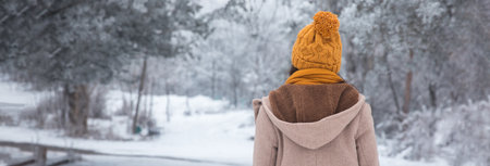 Woman in winter clothing walking in snow on road in the forestの写真素材