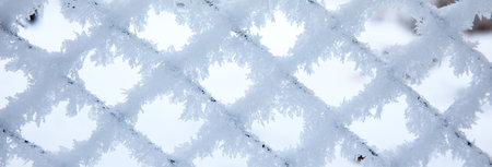 Frozen fence made of metal mesh covered with snowy hoarfrostの写真素材