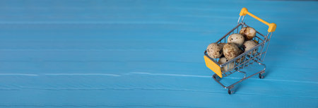 Raw quail eggs in mini shopping cart on blue bakgroundの写真素材