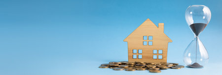 stack of coins with house model and hourglass on table
