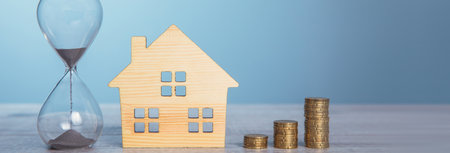 stack of coins with house model and hourglass on tableの写真素材