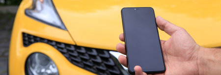 Man holding cell phone with car in background.