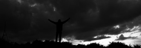 Man standing with raised hands and dark stormy sky.の写真素材