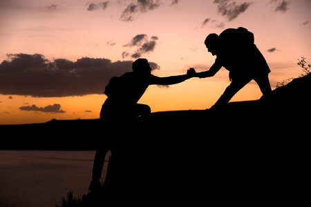 mountain climbers help each other to climb the mountain, sunset, helping a friend. stock photoの写真素材